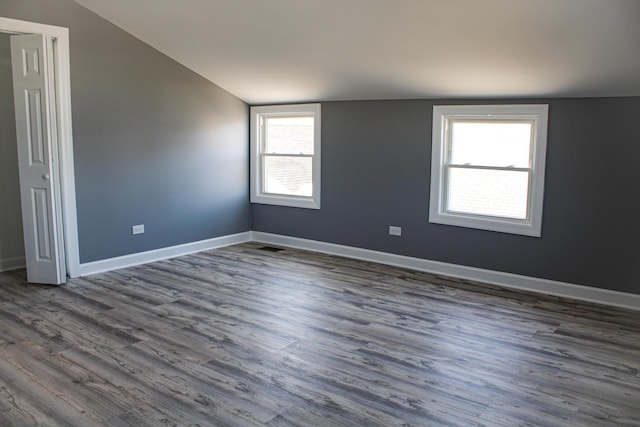 spare room featuring lofted ceiling, dark wood-style flooring, and baseboards