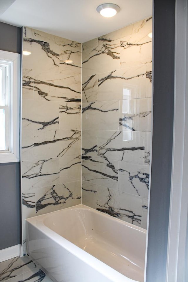 bathroom with marble finish floor and washtub / shower combination