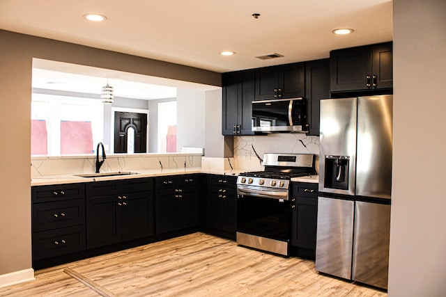 kitchen with stainless steel appliances, dark cabinetry, a sink, and light countertops