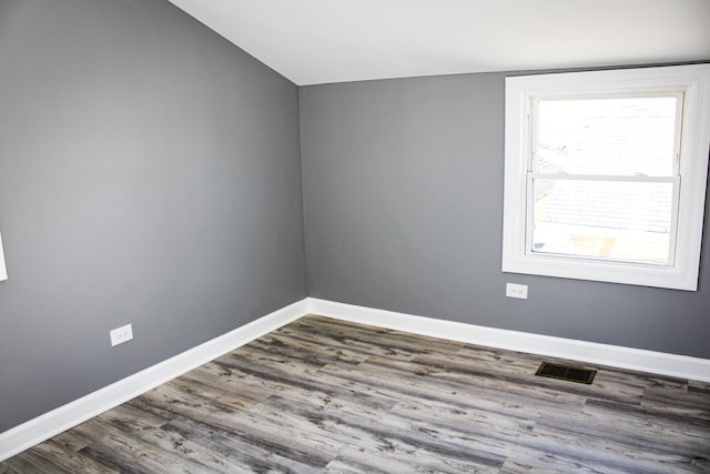 empty room featuring lofted ceiling, visible vents, dark wood finished floors, and baseboards