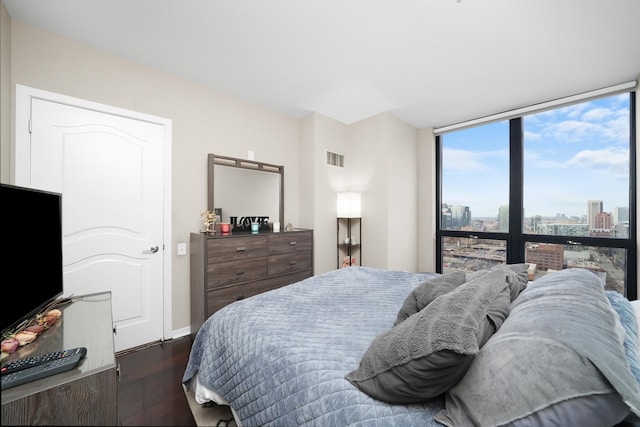 bedroom with dark wood-style flooring, visible vents, baseboards, a view of city, and a wall of windows