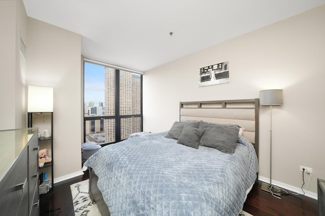 bedroom with a city view, dark wood-style flooring, a wall of windows, and baseboards