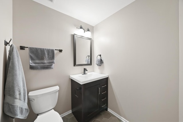 half bath featuring tile patterned floors, vanity, toilet, and baseboards