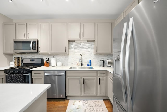 kitchen with dark wood-style flooring, a sink, light countertops, appliances with stainless steel finishes, and backsplash