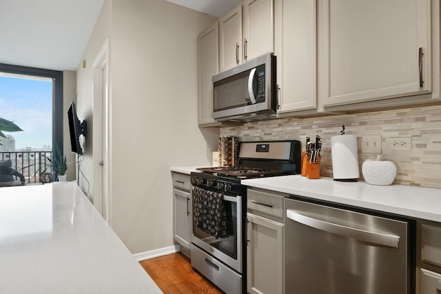 kitchen with wood finished floors, light countertops, appliances with stainless steel finishes, and backsplash