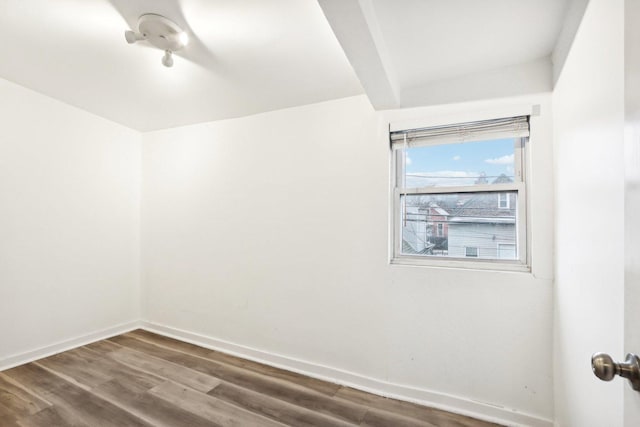 empty room featuring baseboards, wood finished floors, and beamed ceiling