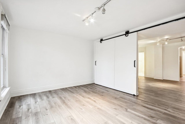 unfurnished bedroom with a barn door, baseboards, light wood-style flooring, and track lighting