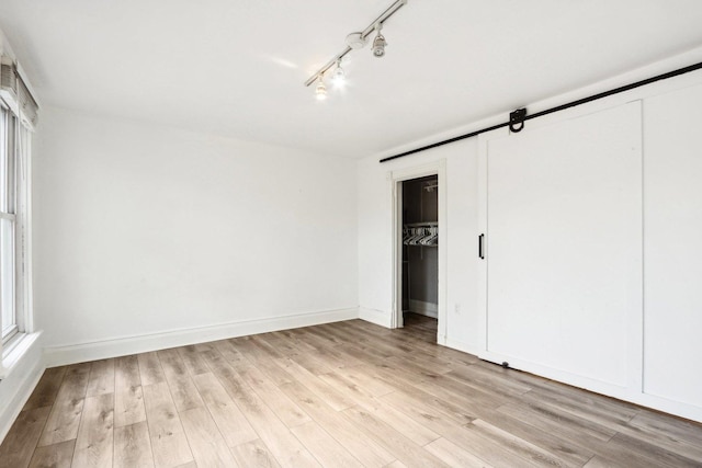 unfurnished bedroom featuring light wood-style floors, a closet, rail lighting, and baseboards