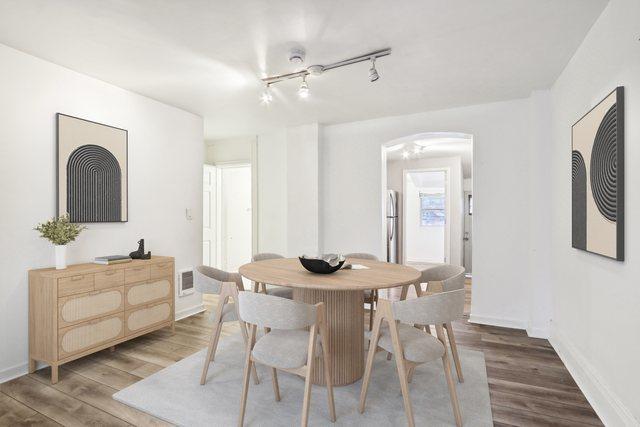 dining room featuring rail lighting, baseboards, arched walkways, and wood finished floors