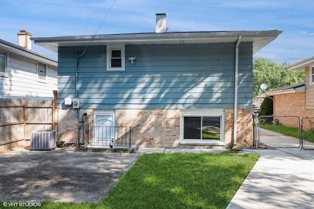 back of property featuring brick siding, a chimney, central AC unit, a gate, and fence