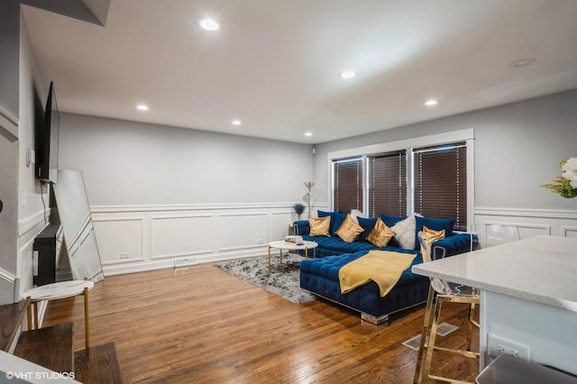 living area with a decorative wall, wainscoting, wood finished floors, and recessed lighting