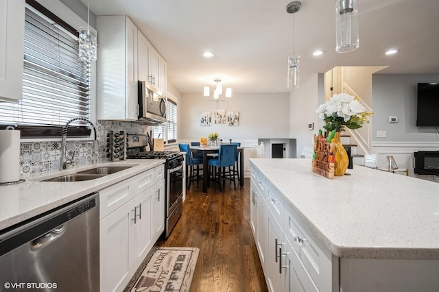 kitchen featuring decorative backsplash, dark wood-style floors, appliances with stainless steel finishes, hanging light fixtures, and a sink