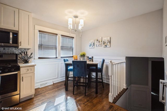 dining room featuring a chandelier, dark wood-type flooring, wainscoting, and visible vents