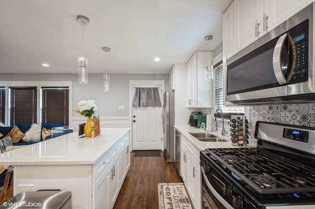 kitchen with white cabinets, appliances with stainless steel finishes, dark wood-style flooring, a center island, and a sink