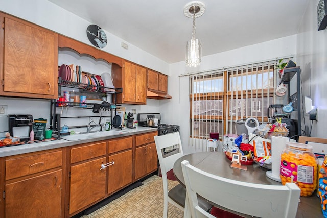 kitchen featuring under cabinet range hood, a sink, range with gas stovetop, light countertops, and brown cabinetry