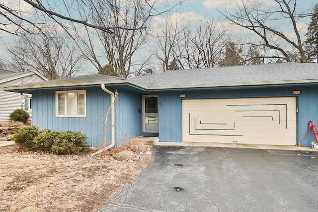 single story home with an attached garage, a shingled roof, and aphalt driveway