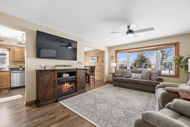 living area featuring dark wood finished floors, a lit fireplace, baseboards, and ceiling fan