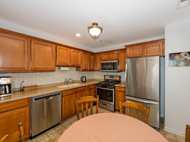 kitchen featuring stainless steel appliances, a sink, visible vents, light countertops, and brown cabinetry