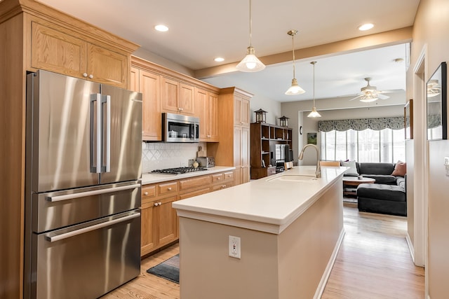 kitchen with stainless steel appliances, tasteful backsplash, open floor plan, a sink, and light wood-type flooring