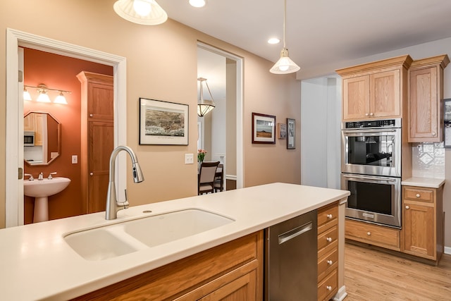 kitchen with light countertops, appliances with stainless steel finishes, a sink, and light wood-style floors