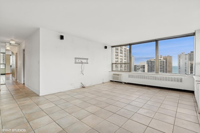 unfurnished room with light tile patterned floors, arched walkways, baseboards, radiator, and a view of city