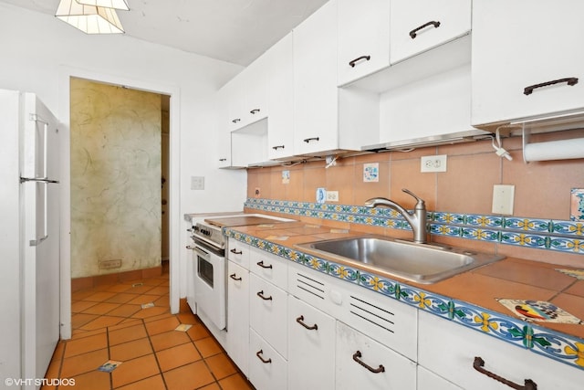 kitchen featuring a sink, white cabinets, backsplash, freestanding refrigerator, and electric range oven