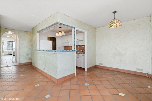 spare room featuring arched walkways, tile patterned flooring, and baseboards