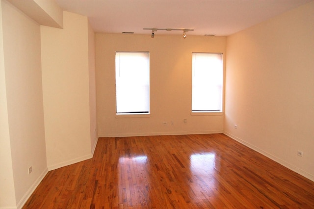 unfurnished room with baseboards, wood finished floors, a healthy amount of sunlight, and track lighting