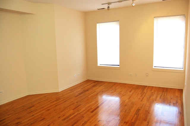 empty room featuring baseboards, visible vents, wood finished floors, and track lighting