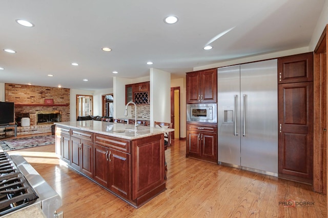 kitchen featuring built in appliances, recessed lighting, a sink, light wood-type flooring, and a brick fireplace