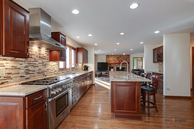 kitchen with wood finished floors, wall chimney range hood, stainless steel range, and a sink