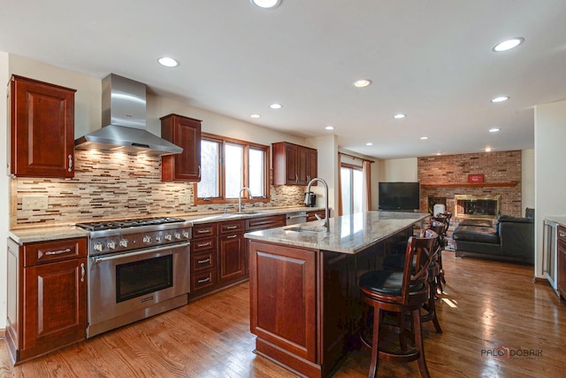 kitchen with stainless steel range, light stone counters, a kitchen breakfast bar, wood finished floors, and wall chimney range hood