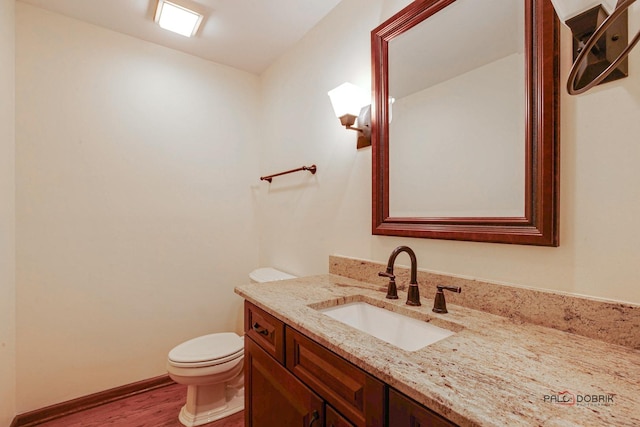 half bathroom featuring baseboards, vanity, toilet, and wood finished floors