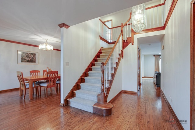 stairway featuring crown molding, a notable chandelier, baseboards, and wood finished floors