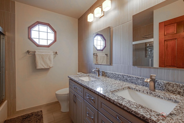 full bath featuring toilet, double vanity, a sink, and a shower with shower door