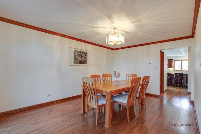 dining room featuring a notable chandelier, ornamental molding, wood finished floors, and baseboards