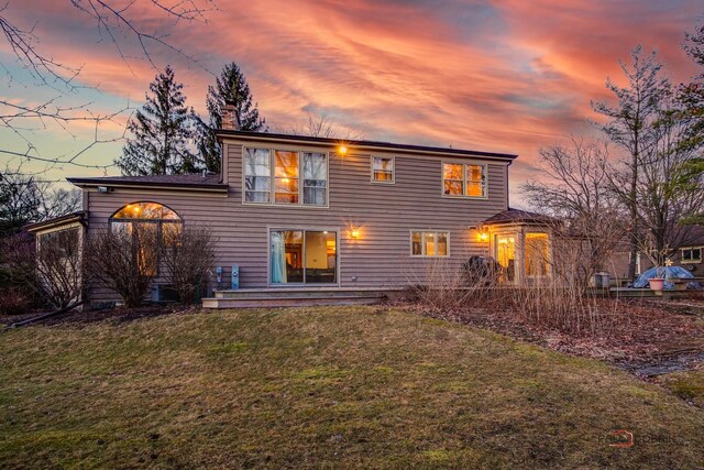 back of property at dusk with a lawn and a chimney