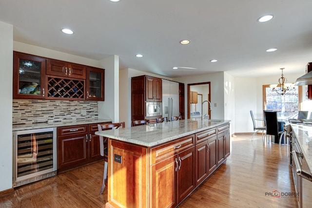 kitchen featuring wine cooler, wood finished floors, built in appliances, a sink, and backsplash