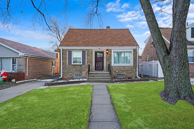 bungalow-style house featuring brick siding, a shingled roof, fence, a chimney, and a front yard