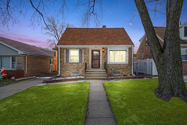 bungalow-style house with brick siding, a chimney, a shingled roof, fence, and a front lawn