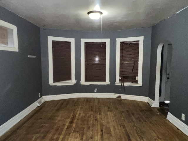 spare room featuring arched walkways, baseboards, and wood finished floors