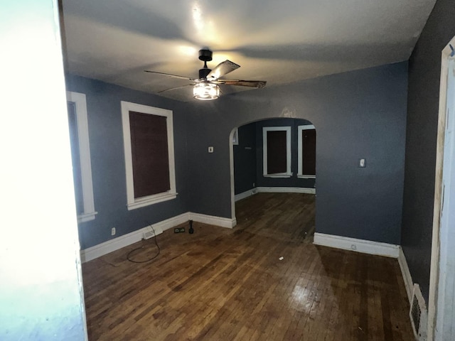 spare room with arched walkways, visible vents, a ceiling fan, baseboards, and wood-type flooring