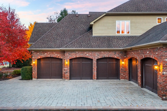 view of front of home featuring a shingled roof, decorative driveway, brick siding, and a garage