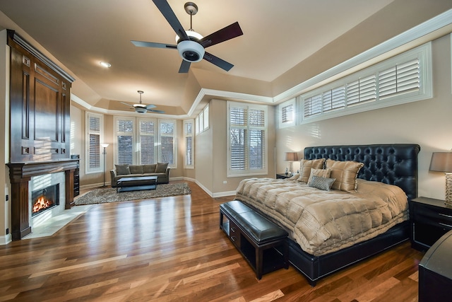 bedroom featuring dark wood-style flooring, a fireplace, a raised ceiling, and baseboards