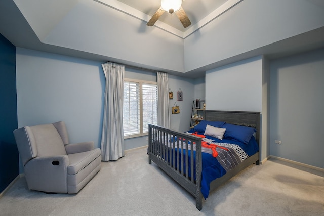 carpeted bedroom with ceiling fan, a raised ceiling, and baseboards