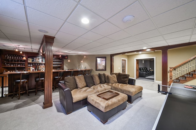 carpeted living area featuring bar area, a drop ceiling, decorative columns, and stairway