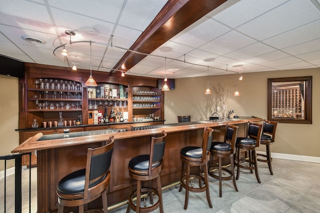 bar with a community bar, baseboards, hanging light fixtures, rail lighting, and a paneled ceiling