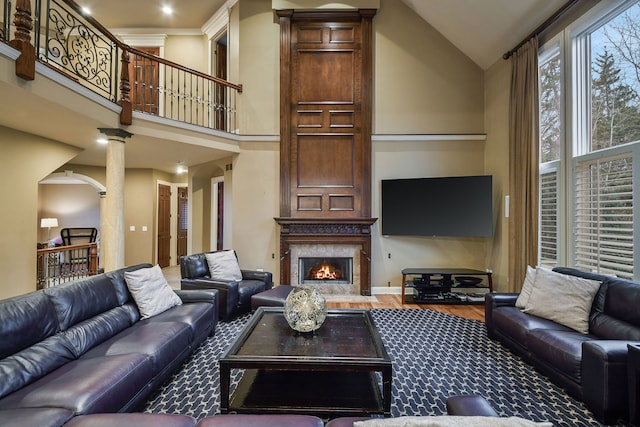 living room with ornate columns, a premium fireplace, high vaulted ceiling, and wood finished floors