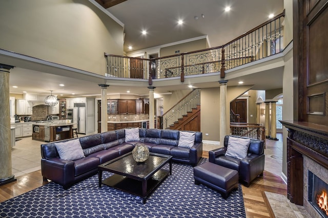 living area with a fireplace, a towering ceiling, stairs, ornate columns, and crown molding