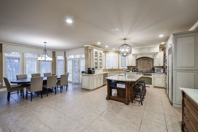 kitchen with a notable chandelier, a sink, a kitchen breakfast bar, a center island with sink, and glass insert cabinets